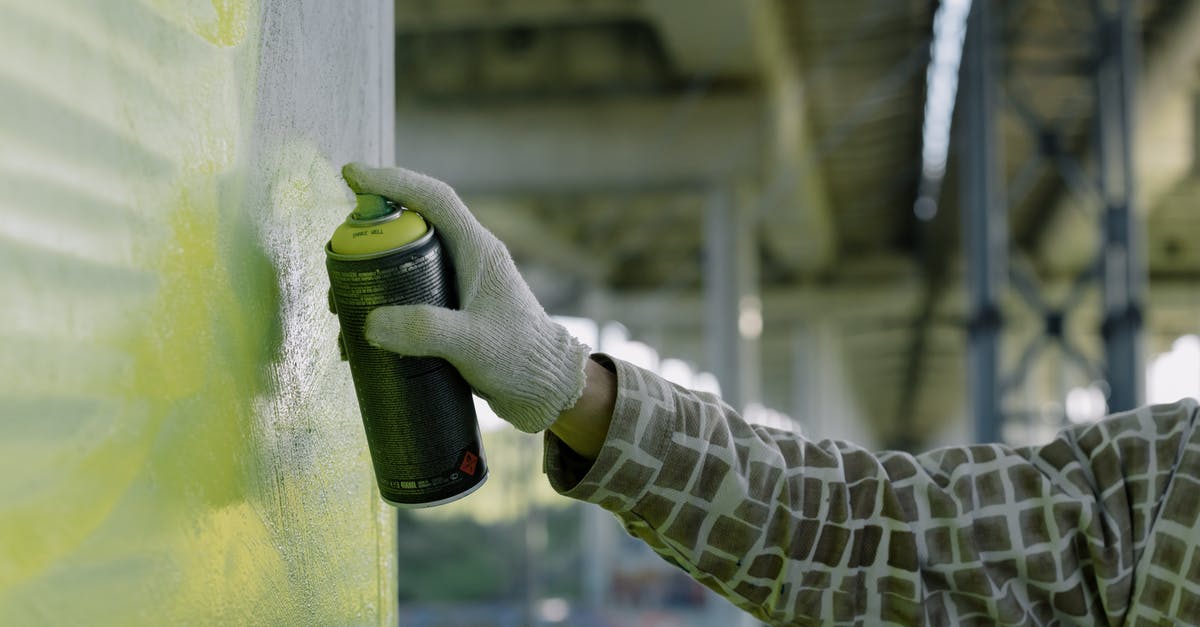 Are aerosol cans allowed and safe, in checked luggage? - A Person's Hand Wearing Gloves Spraying Paint on Concrete Wall