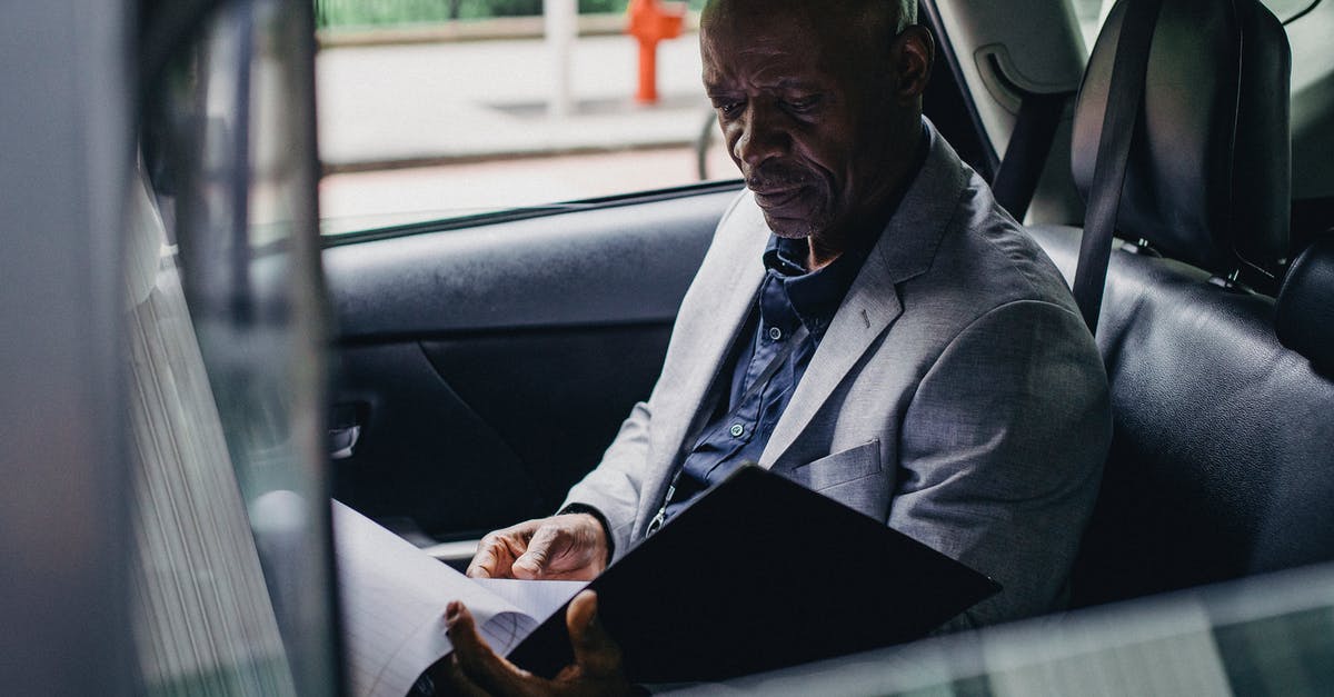 Are car rental contracts provided in English? - Side view serious African American businessman in formal clothes sitting in car back seat and reading documents