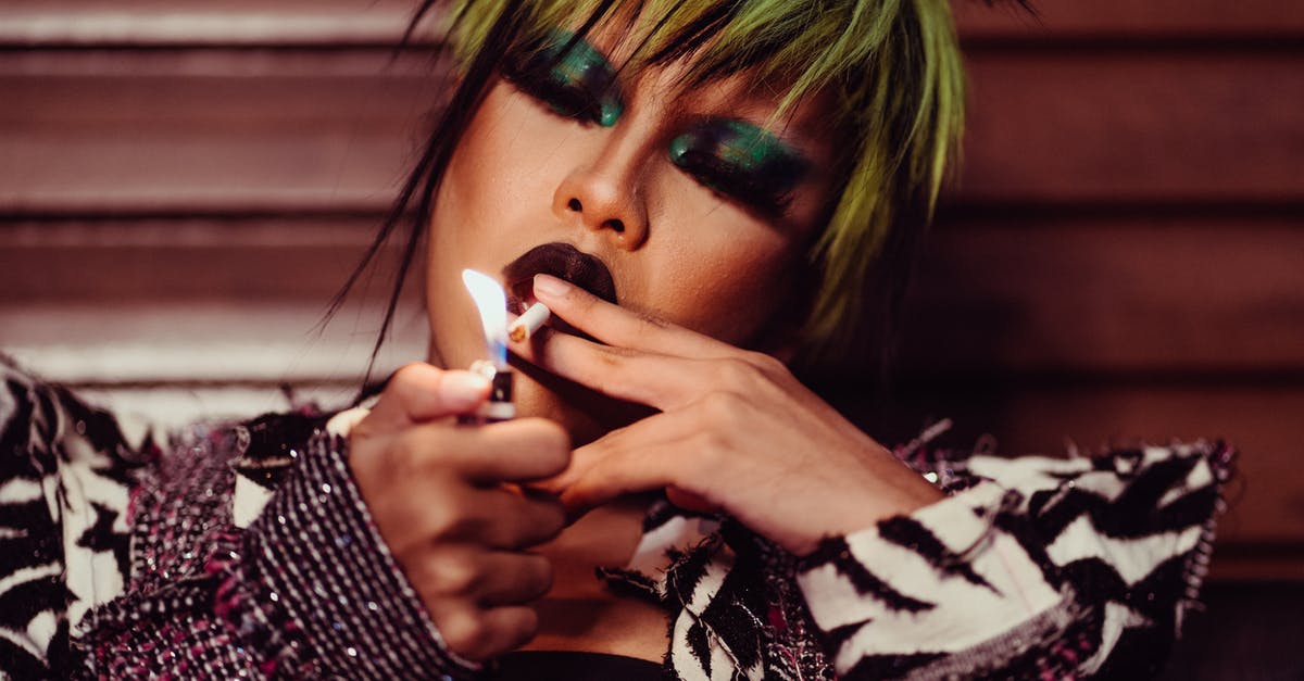 Are cigarette lighters allowed in airports? [closed] - Crop male crossdresser model with colorful makeup and modern hairstyle holding lighter while smoking cigarette with closed eyes