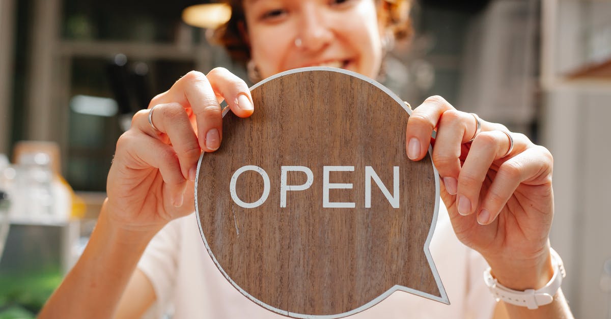 Are Parisian shops open on Sundays? - Happy young woman worker in casual clothes standing in light cafe and showing small sign with word open