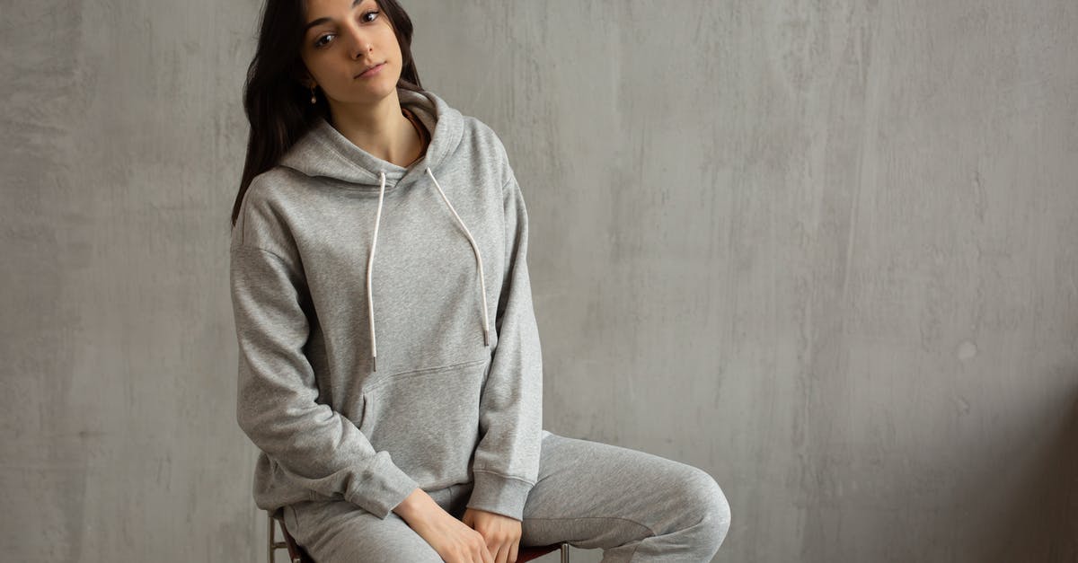 Are sweatpants frowned upon on flights? - Young female in gray sports suit sitting on chair against concrete wall and looking at camera