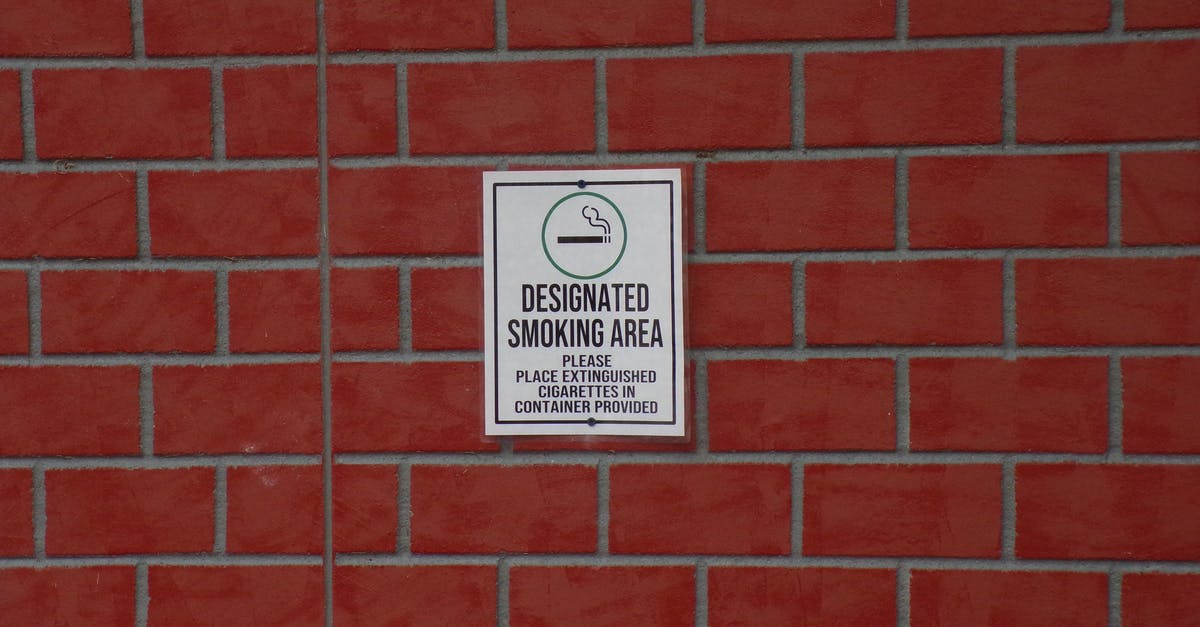 Are there any airlines that still allow smoking on-board flights? - Building with brick wall and signboard with title indicating smoking area with symbol of cigarette