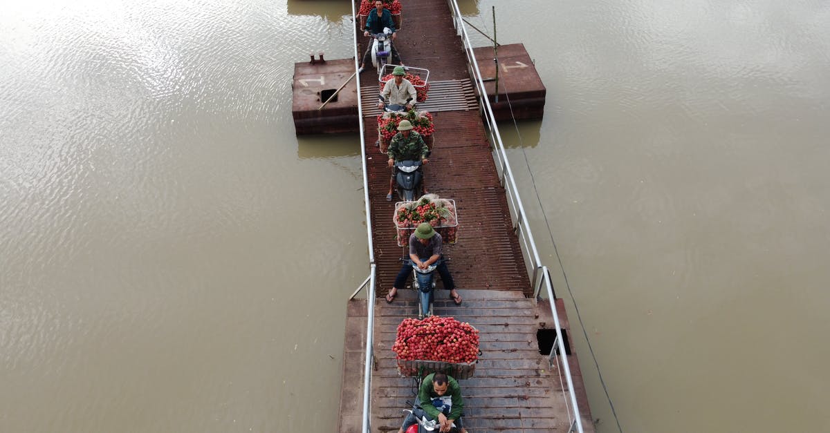 Are there any countries in South-East Asia that don't require a motorcycle licence to ride one? - From above of people transporting food in baskets on motorbikes riding on float bridge above rippled river
