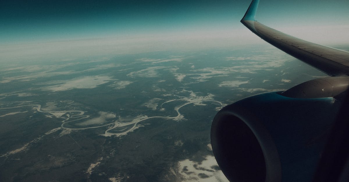 Are there any flights which fly above the Bermuda Triangle? - Through window of modern wing and turbine of airplane flying in sky above verdant land