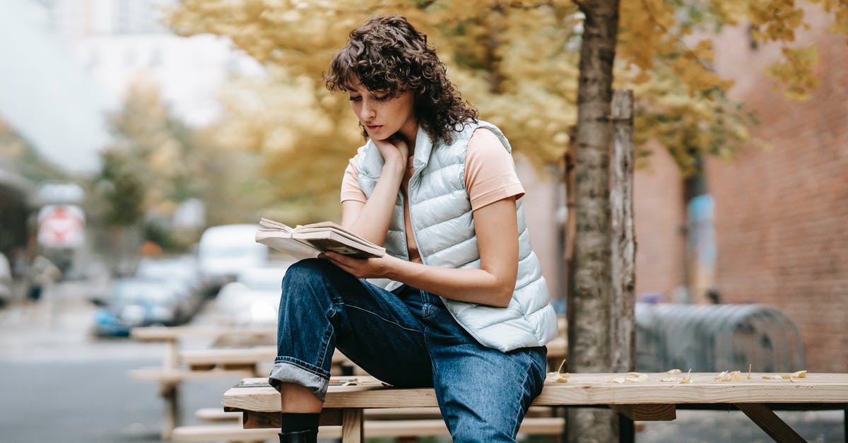 Are there any genuine gers near Sydney? - Pensive female in trendy outfit reading book while sitting on wooden table near autumn tree on city street in daytime