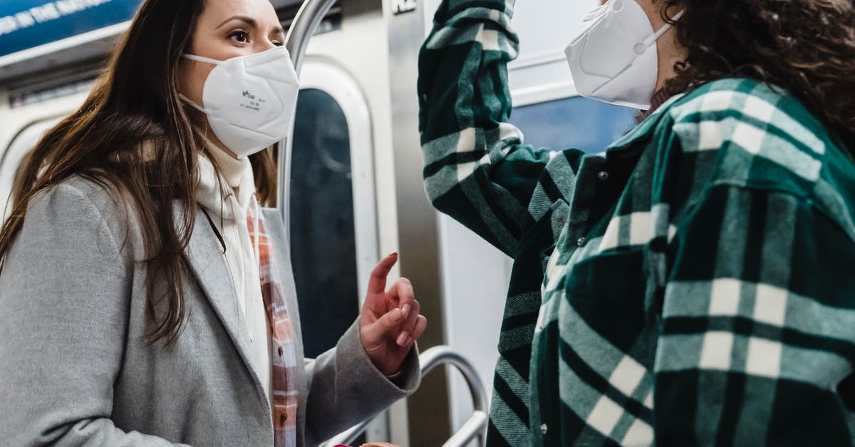 Are there any passenger trains from Sweden to Finland? - Low angle side view of multiracial female friends in protective masks looking at each other while riding in subway wagon