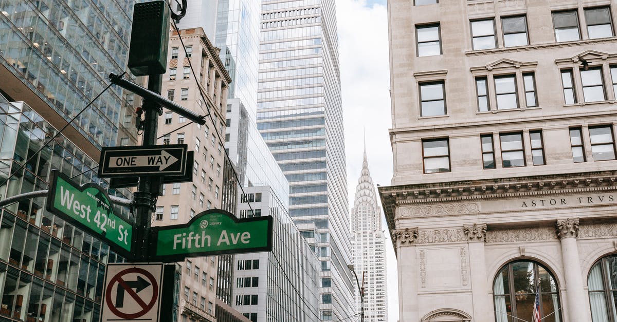 Are there any resorts in the NYC area? - Low angle of road sign on pillar with traffic light located in city on avenue with modern skyscrapers and residential buildings