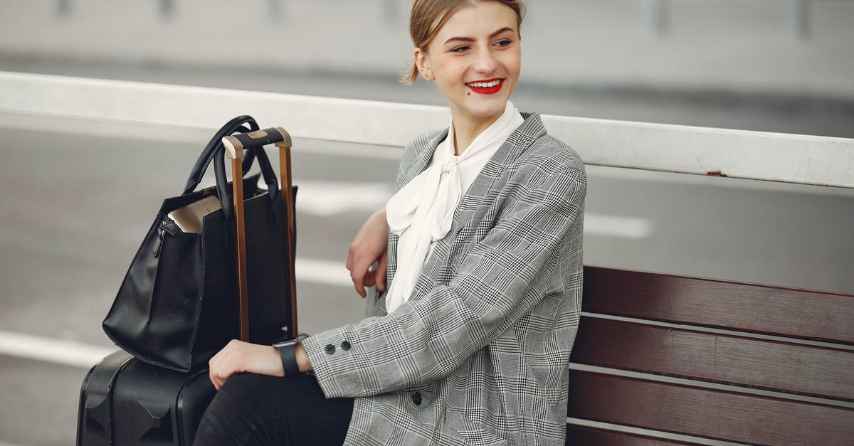 Are there any rest areas in Dubai's Terminal 3? - Positive female traveler in trendy clothes smiling away while waiting for train sitting on wooden bench with suitcase and bag in street