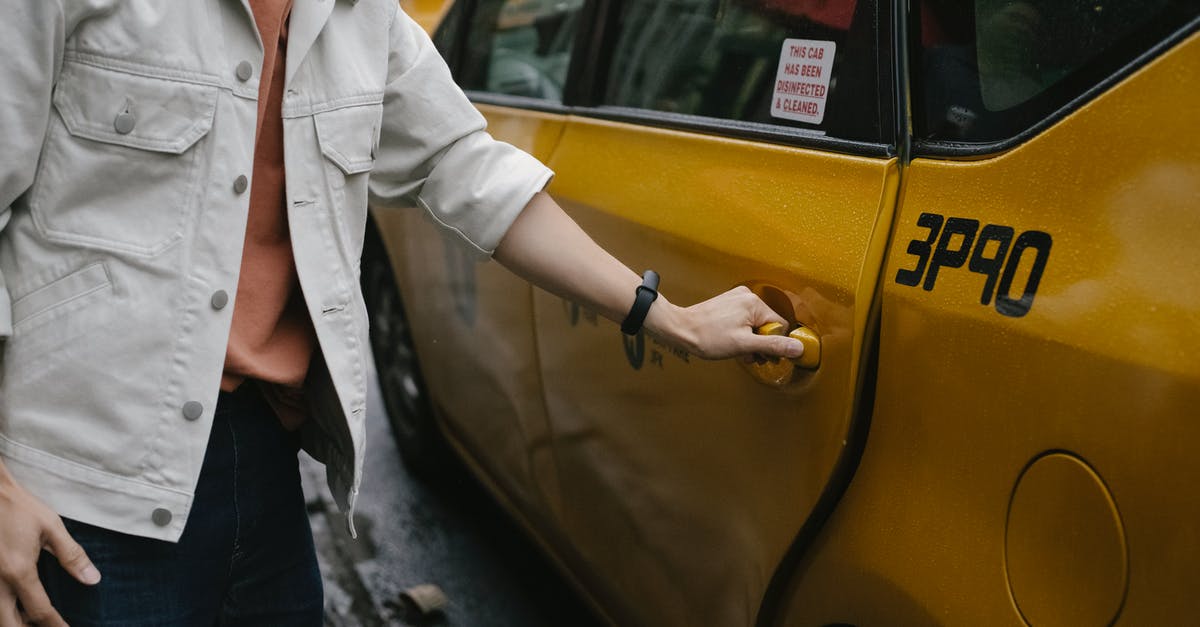 Are there any self-driving cab services in India - Unrecognizable passenger in casual clothes opening door of cab parked on roadside in city on street while commuting to work