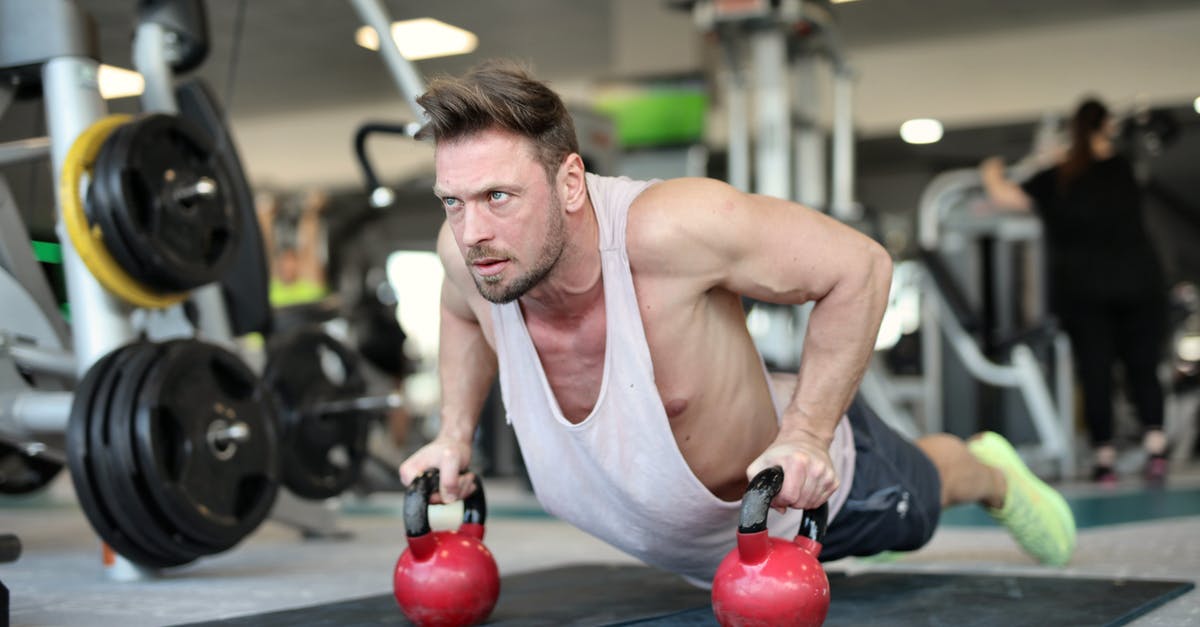 Are there metal clubs in London? - Low angle of strong sportsman making effort and pushing up on metal kettlebells during workout in modern gym and looking away