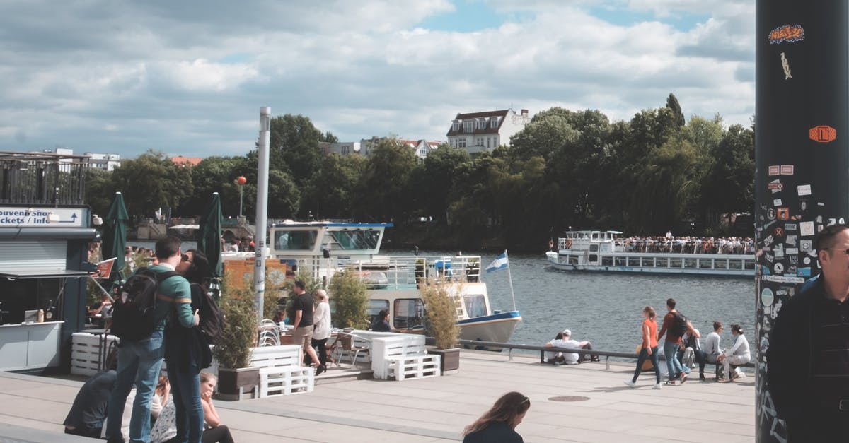 Are there still many refugees on the Copenhagen-Hamburg train? - Crowd of people walking at port with ships near tranquil rippling river under cloudy sky in daytime