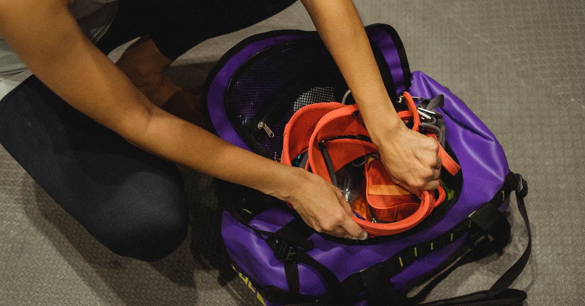 Are workstation monitors safe to pack in checked luggage? - From above of crop anonymous female athlete sitting on floor and packing safety belt in bag after training in contemporary gym