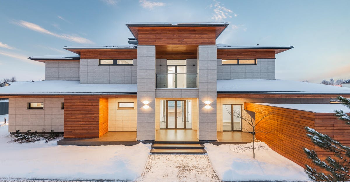 Arriving at a Schengen country with a Schengen visa - Backyard view of new modern luxurious cottage house with stone and wooden facade and illumination in winter countryside