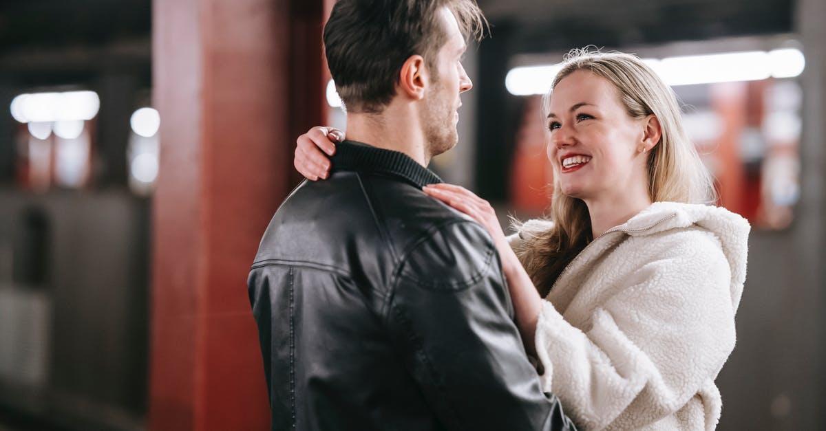 Arriving Before Visa Start Date - Smiling couple looking at each other and embracing while standing on platform of metro with train on blurred background during date