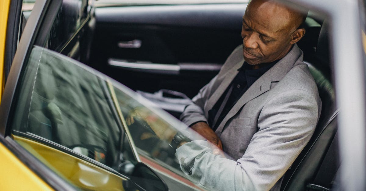 Arriving very late at hotels in Athens - Side view punctual adult African American businessman in formal clothing sitting in taxi car and checking time on wristwatch