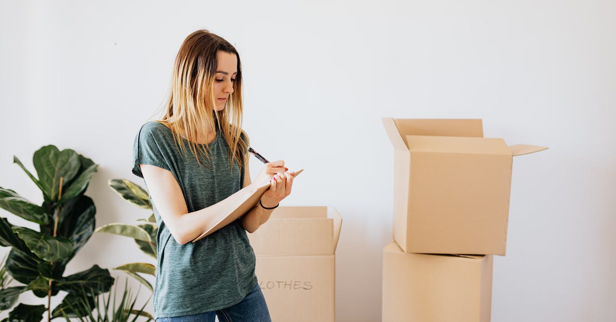 At JFK, can you move between terminals airside on domestic flights? - Focused young lady in casual wear taking notes in clipboard while standing near packed carton boxes before moving into new house