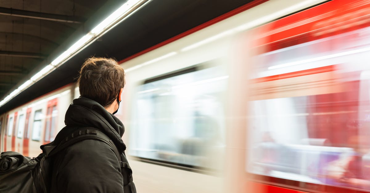 Azerbaijan eVisa - Arrival by Train - Side view of faceless male passenger in protective mask wearing warm outerwear standing on platform of metro station near train