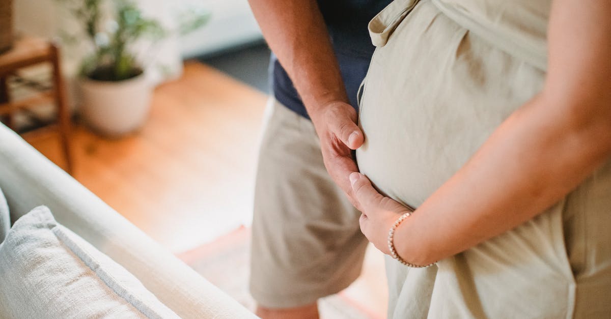 B2 tourist visas for my future wife and her parents - From above of crop faceless couple in casual outfit standing in light living room and touching pregnant belly gently