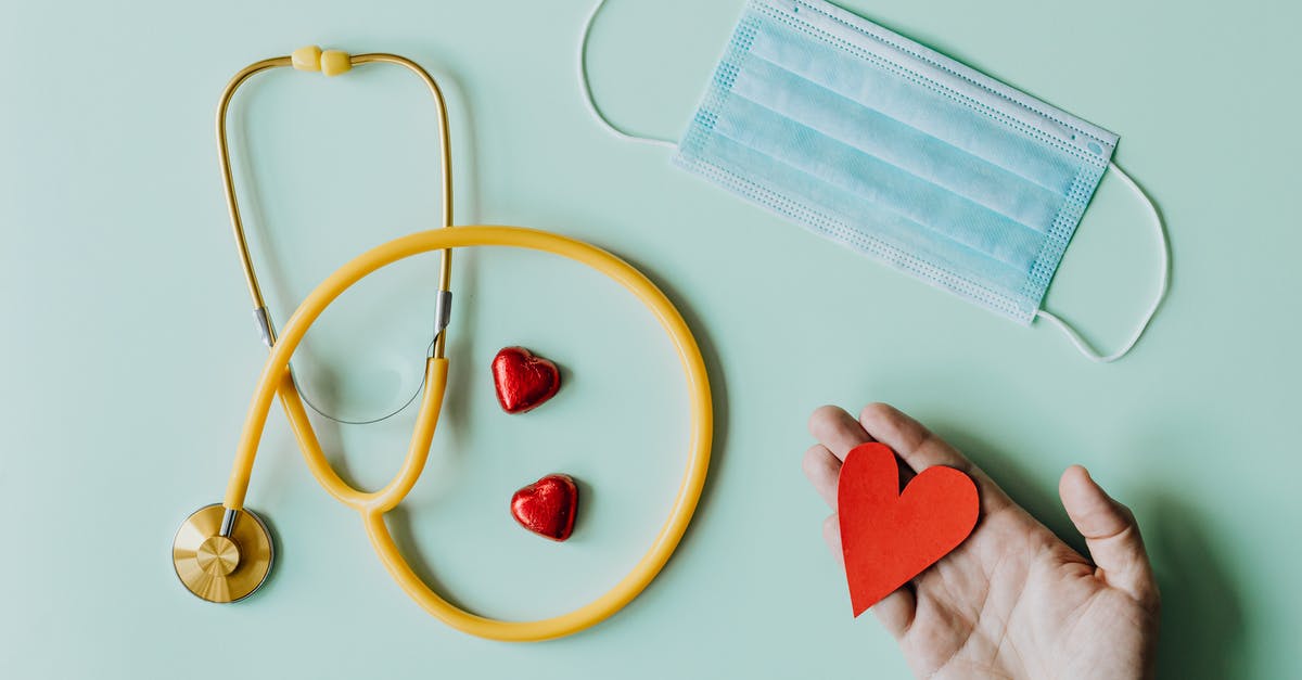 B2 visa extension due to covid - Top view of crop anonymous person hand with red paper heart on table with stethoscope and medical mask for coronavirus prevention