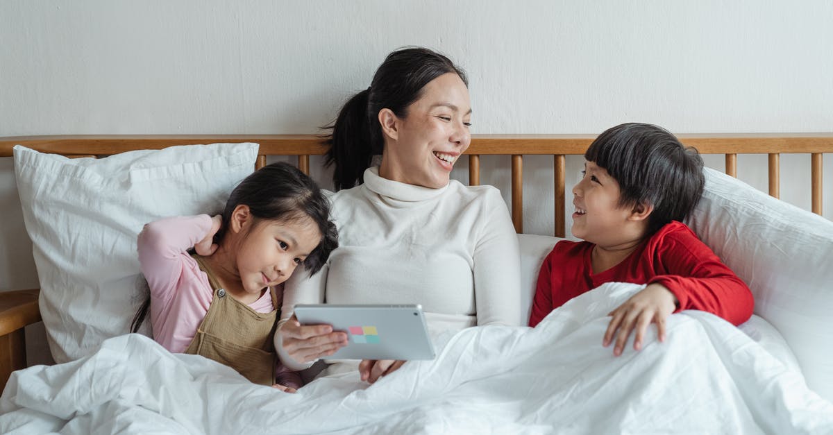 B2 visa extension online for parents [closed] - Positive ethnic mother and little daughter and son having fun together in cozy bed in morning while using tablet