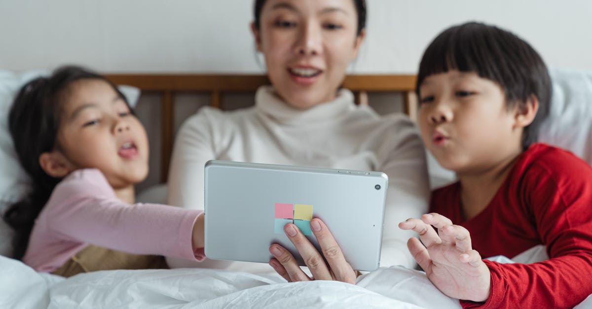 B2 visa extension online for parents [closed] - Interested Asian mother and little daughter and son in pajamas lying in comfortable bed choosing content in Internet on tablet while spending time together in morning