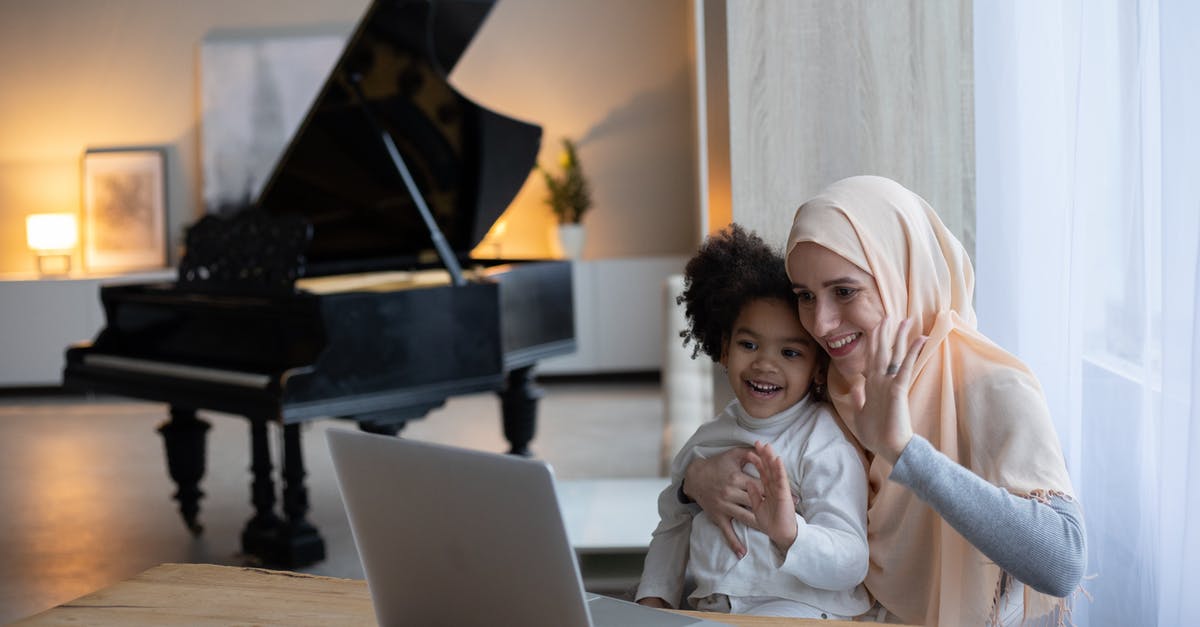 B2 visa extension online for parents [closed] - Positive Muslim mother and adorable African American girl sitting at table near window and having video call on portable laptop