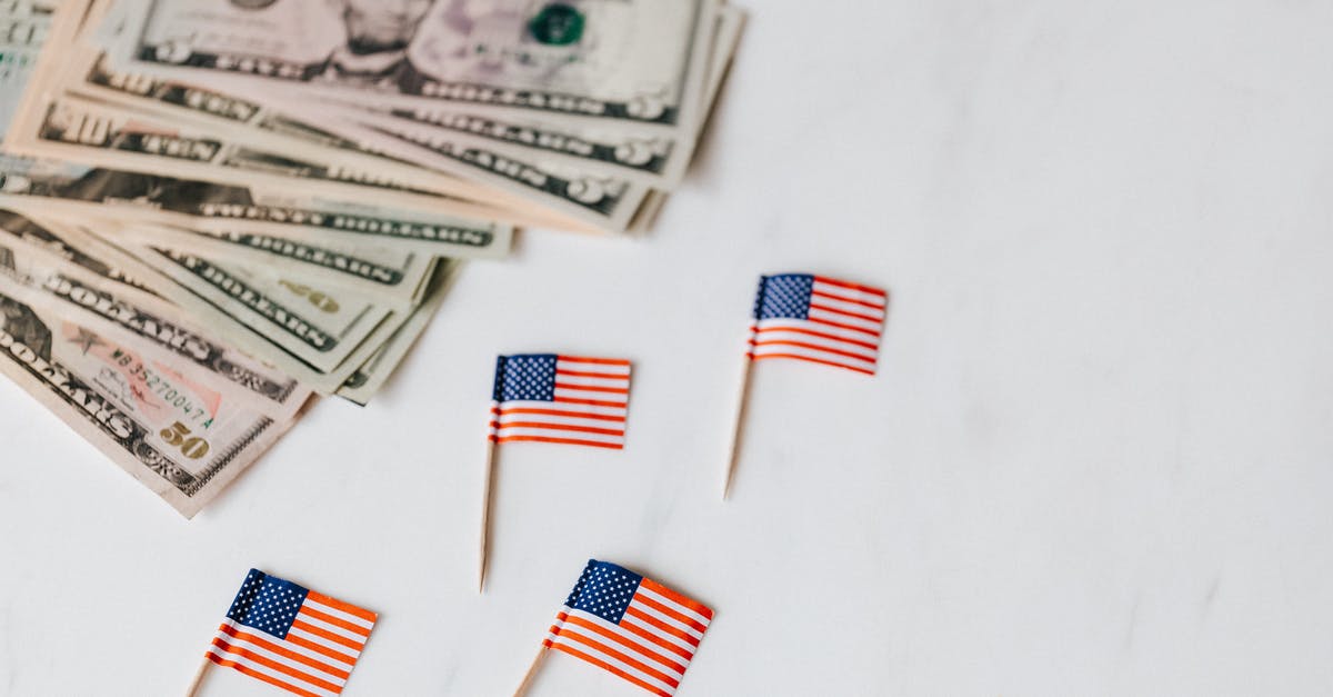 Baby with passport from different country than his parents - From above of flags of United States of America on toothpicks placed near bundle of American dollars of different nominal pars on white surface of table