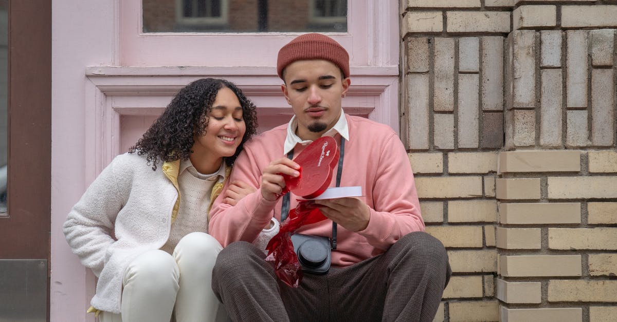 Backpacking Jamaica in February [closed] - Young ethnic guy in stylish outfit opening heart shaped box with chocolate while sitting on street with happy excited girlfriend on Saint Valentines Day