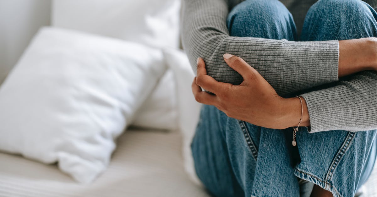 Bad hostel, recourse? - Crop faceless female feeling helpless and frustrated embracing knees while sitting on bed in loneliness