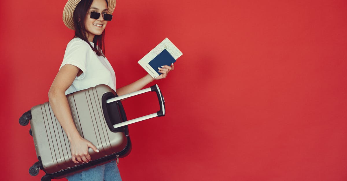 Baggage allowance inquiry with two different airlines in one ticket - Side view of cheerful young woman with passport and tickets smiling and looking at camera while walking with baggage on red background