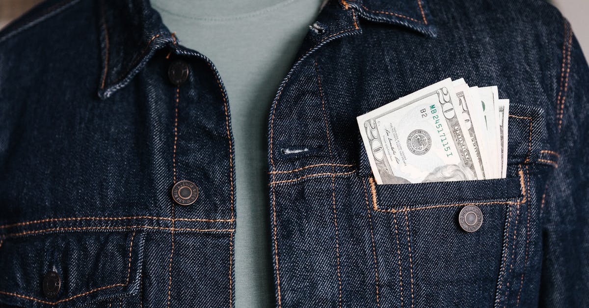 Baggage charge price difference based on country of origin - Crop unrecognizable male in casual outfit standing with different nominal pars of dollar banknotes in pocket of jeans jacket