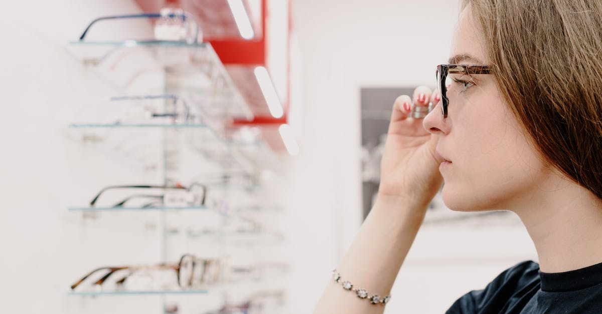 Baggage charge price difference based on country of origin - Side view of crop concentrated female customer putting on eyeglasses for improving eyesight while choosing rim in shop