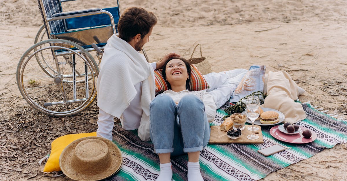 bags and wheelchair - Couple Sitting on Green and Blue Mat on Beach