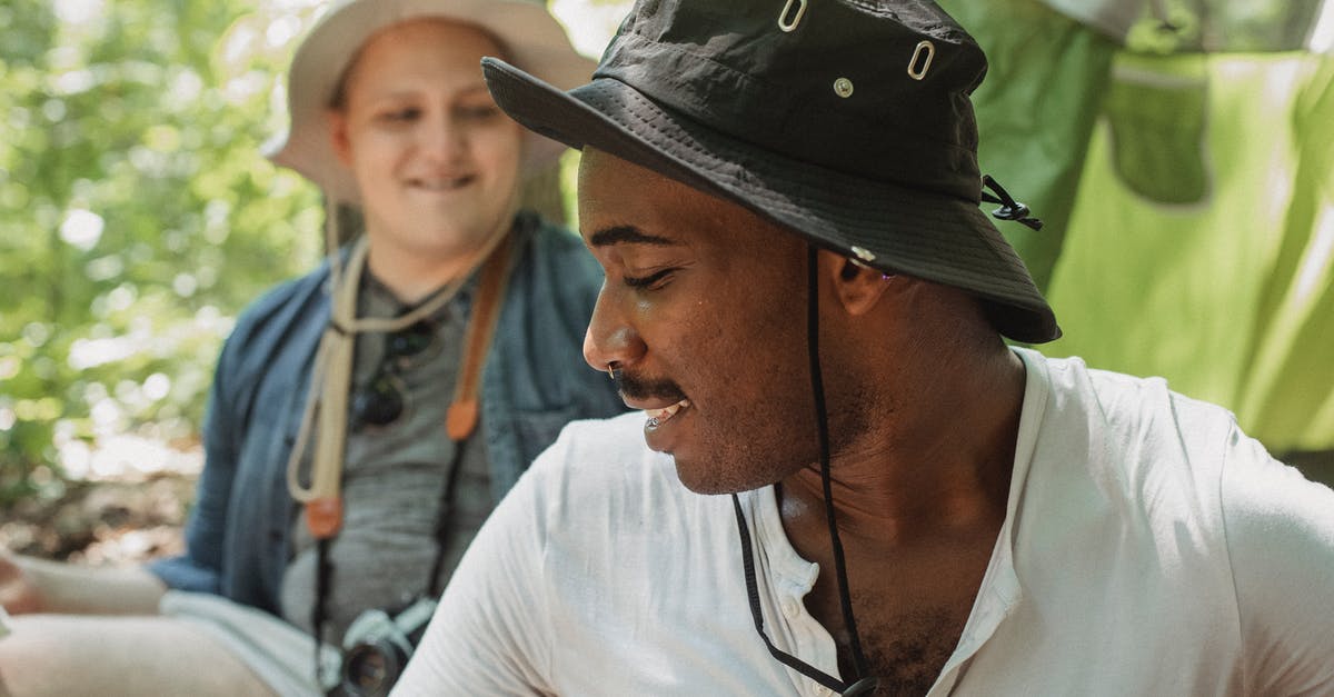 Basic campsites in Black Forest (Schwarzwald) [closed] - Cheerful African American guy sitting near tent in forest and chatting with friend during hike trip