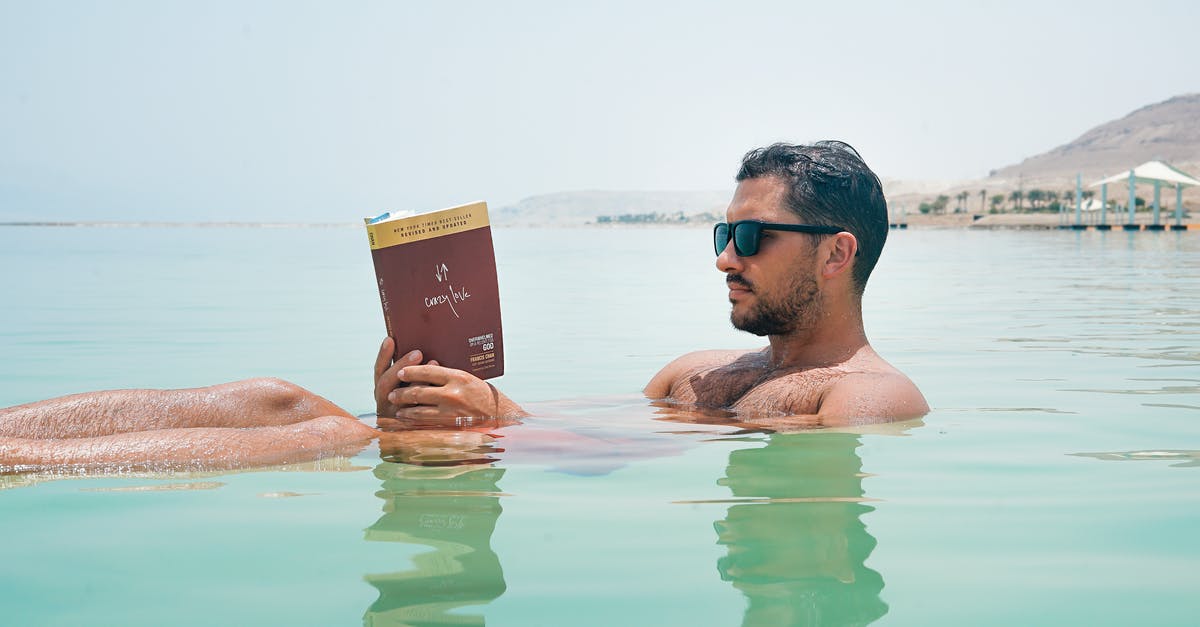 Beef jerky to Israel - Man Wearing Sunglasses Reading Book on Body of Water