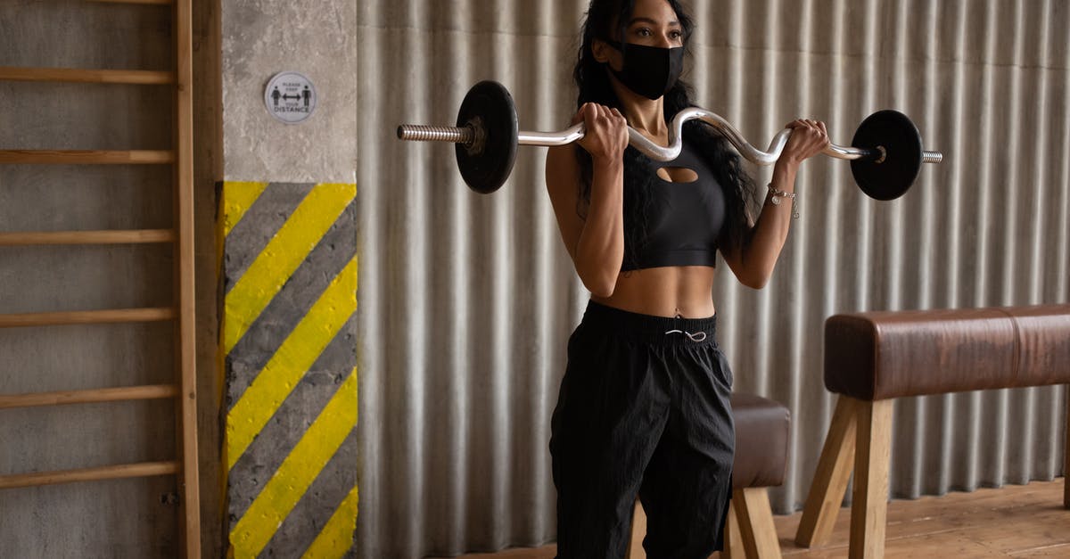 Best practice for managing Covid vaccination documentation - Black sportswoman in face mask exercising with barbell in gymnasium