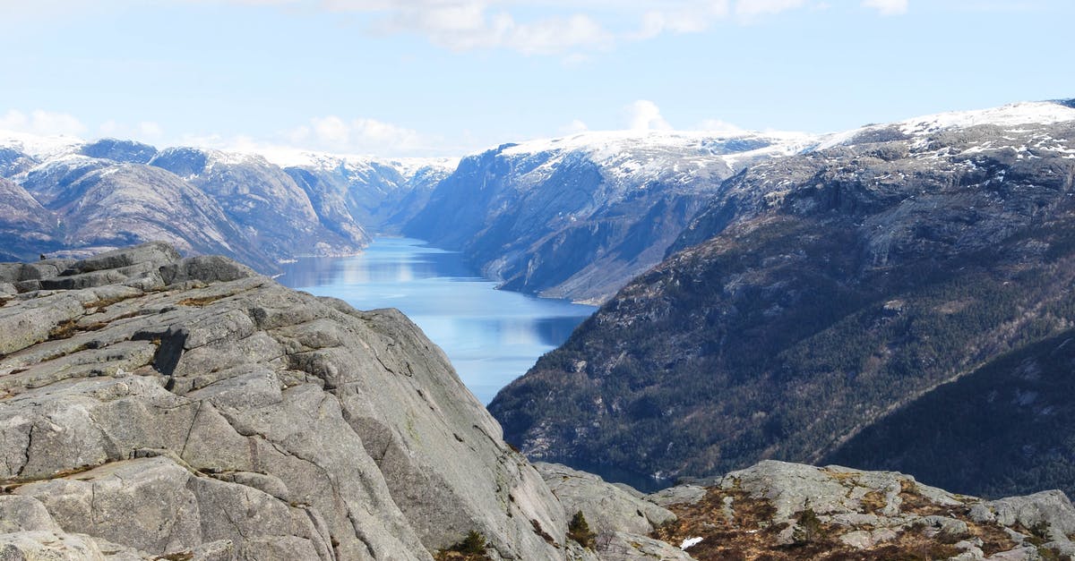 Best season for Norway fjords cruise? - Breathtaking view of calm cold lake surrounded with rocky hills covered with snow under blue sky