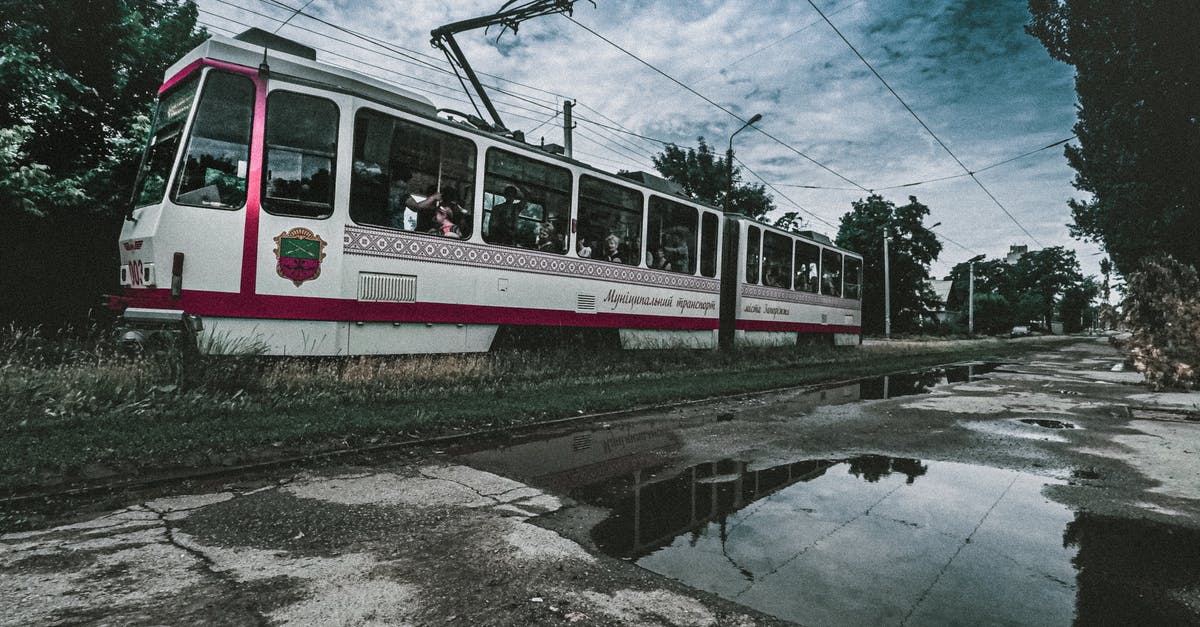 Best way to leave EU with expired visa - Tram riding on railroad near puddles of water and green trees under cloudy sky