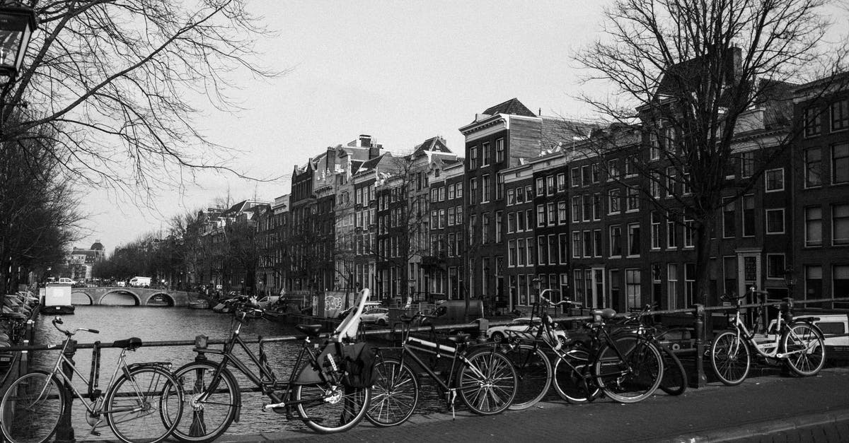 Bicycle rental in Netherlands with drop-off in another city - Black and white of various bicycles parked on paved bridge over rippling canal near aged typical residential buildings in Amsterdam