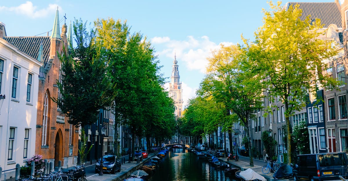 Bicycle rental in Netherlands with drop-off in another city - Perspective view of peaceful narrow canal street in Amsterdam with typical small houses on sunny spring day