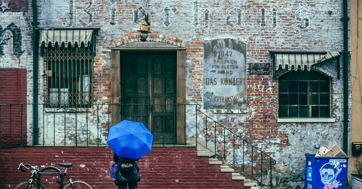 Bike location multi-destination California - Back view of unrecognizable traveler in warm clothes in backpack and umbrella in hand standing on street near aged historical brick building during sightseeing tour in city