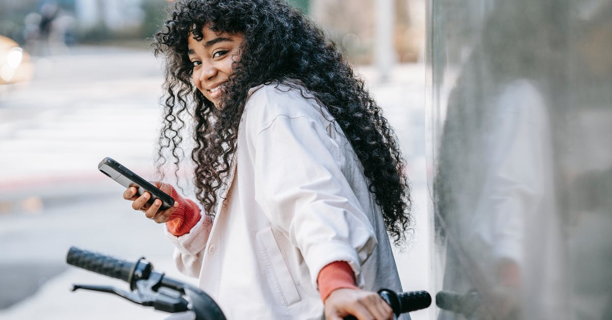 Bike sharing apps-rent cycle in one and back in other city - Cheerful black woman with bicycle using smartphone on street