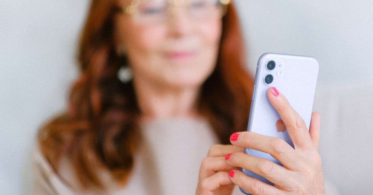 Boarding passes and online check-in - Crop aged redhead female in eyeglasses using contemporary mobile phone while surfing internet in soft focus