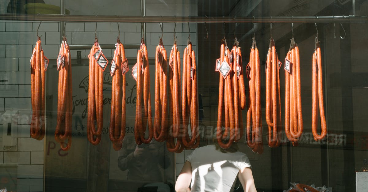 Boarding passes when going through long layovers / stopovers? - Through glass back view of unrecognizable worker in white T shirt at meat preserving factory with long sausages hanging from metal rail in tiled room