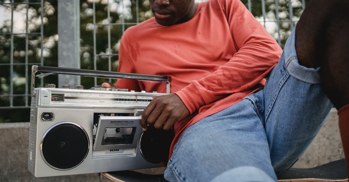 Boarding point change for an Indian rail reservation - Crop black man in casual clothes opening retro recorder to change cassette during resting on concrete surface with skateboard in city street