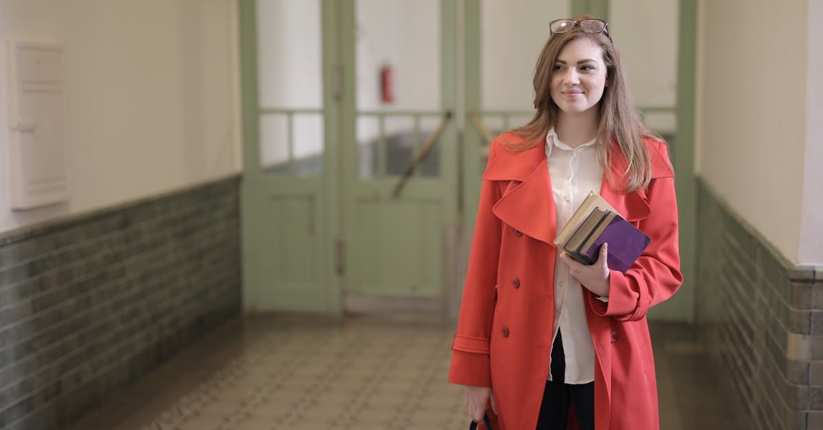 Book Now or Wait [closed] - Young clever woman in classy outfit standing in university corridor with stack of books and bag while waiting for lesson and looking away