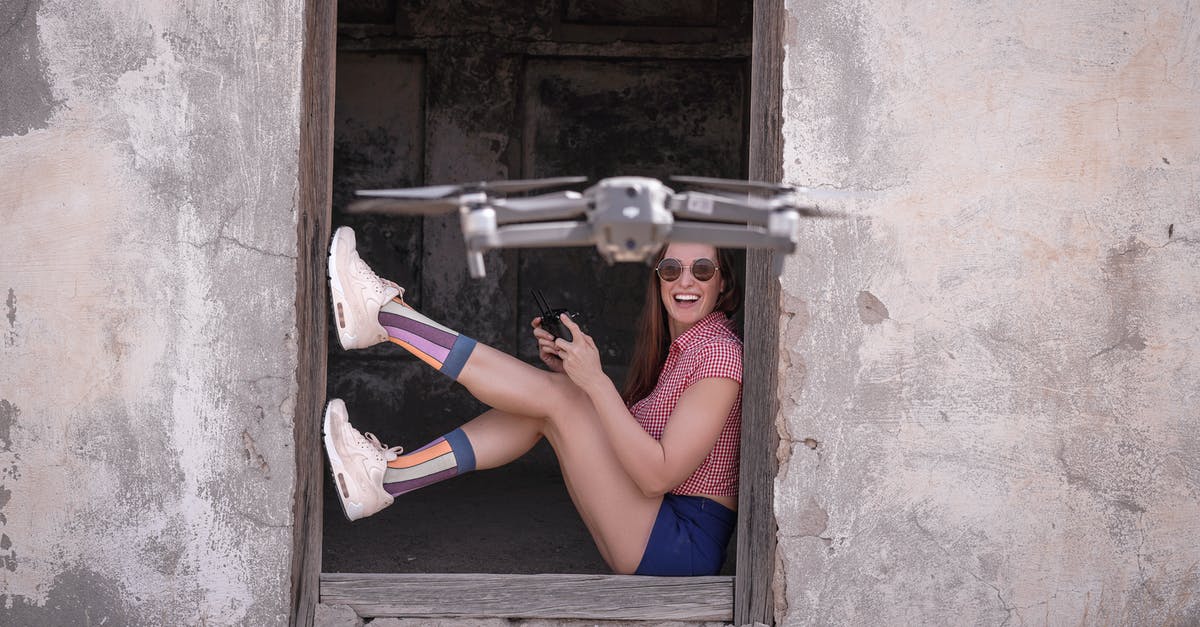 Booking a backup flight for short layover - Side view full body excited female in casual wear sitting at remaining hut entrance and operating modern drone