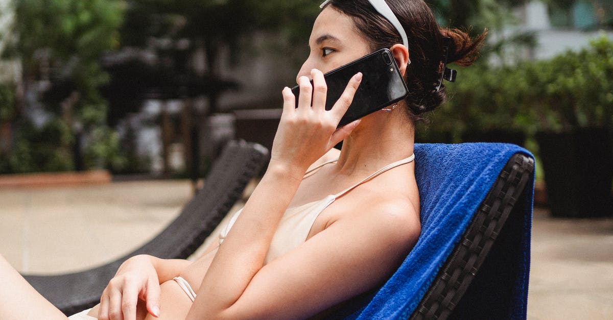 Booking.com didn’t call hotel to cancel should I be worried? - Young slim ethnic lady talking on mobile phone while sitting on sunbed in hotel yard