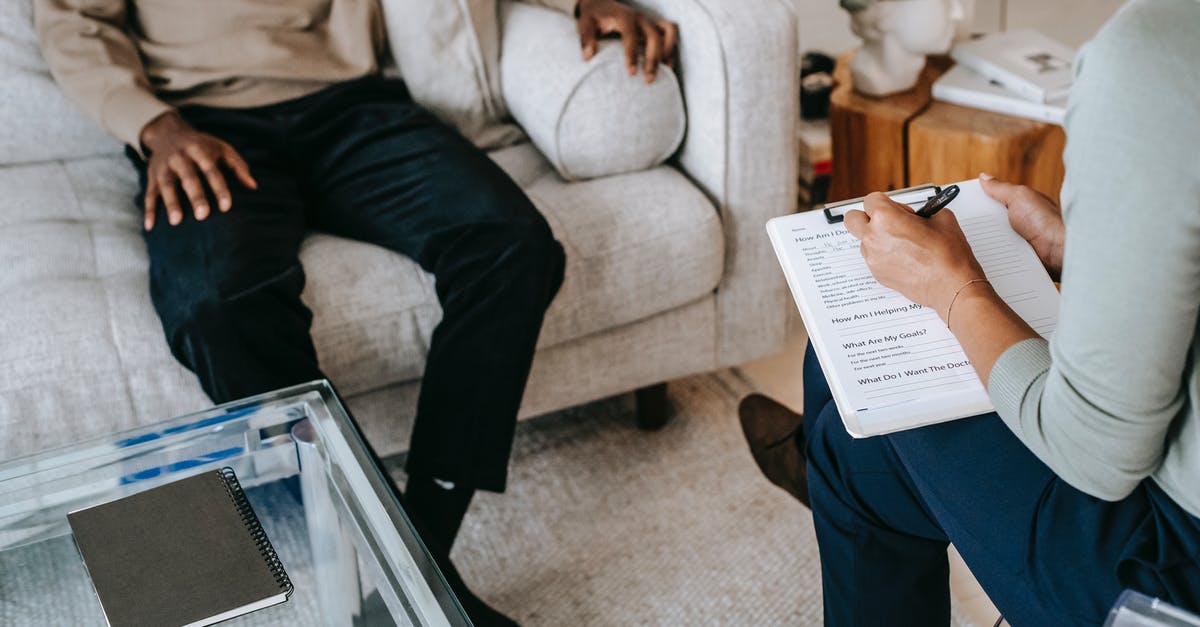 Border visit to China from Uttarakhand, India? - From above crop African American male in casual clothes sitting on comfy couch and answering professional female consultant questions in modern psychotherapy office