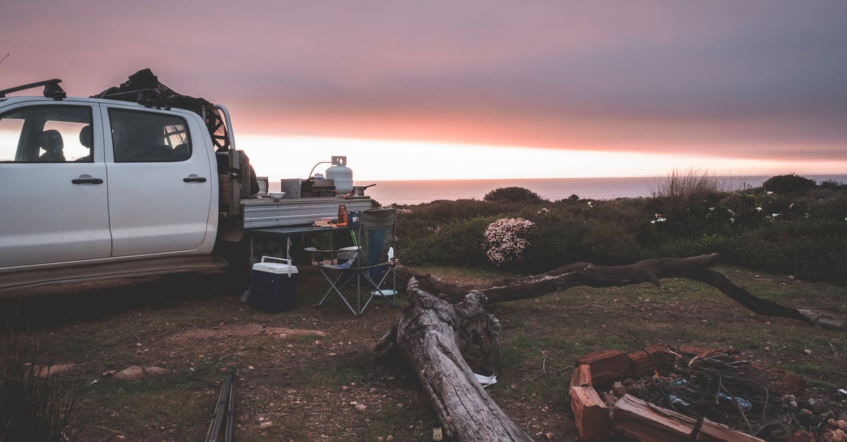 Breaking down with car during trip - multiple country breakdown service? - Modern pickup truck parked on glade near unfolded travel chair table and round bonfire place in peaceful vast nature under amazing evening sky